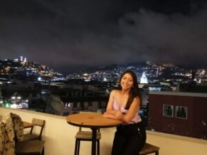 Maritza sentada en una terraza con vista nocturna al centro histórico de Quito.