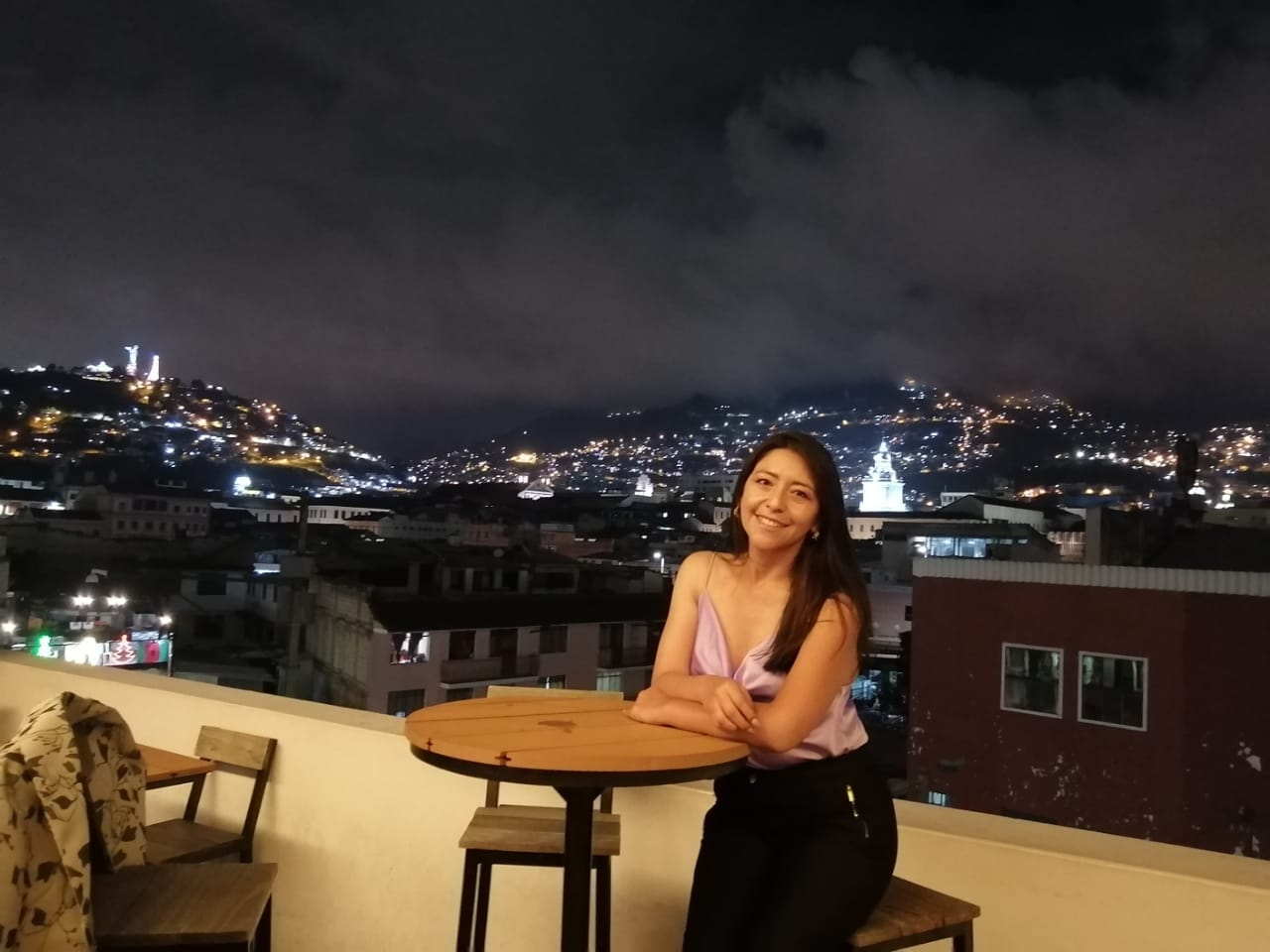 Maritza sentada en una terraza con vista nocturna al centro histórico de Quito.